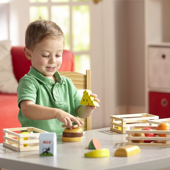 Child playing with wooden food pieces including cheese and burger from the Food Groups set with sorting baskets.