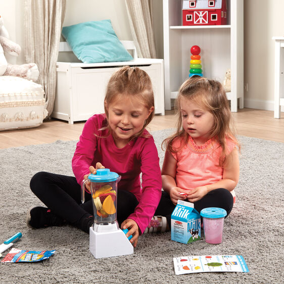 Two children playing with the Smoothie Maker Blender Set including blender, milk carton, and menu card on carpet.