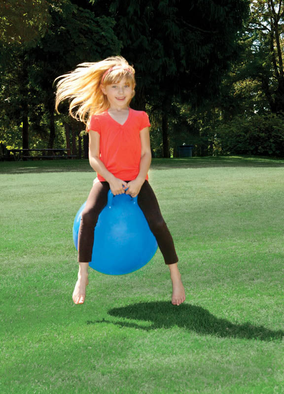 Young girl joyfully bouncing on a blue Hoppy Ball outdoors on green grass in a sunny park setting