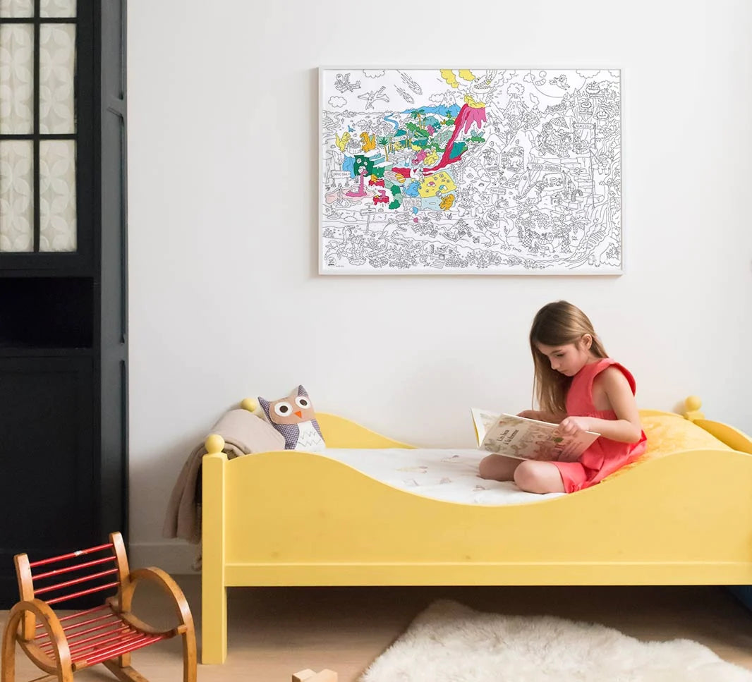 Child reading in yellow bed beneath a partially colored Dinosaur Giant Coloring Poster on the wall in a cozy room.