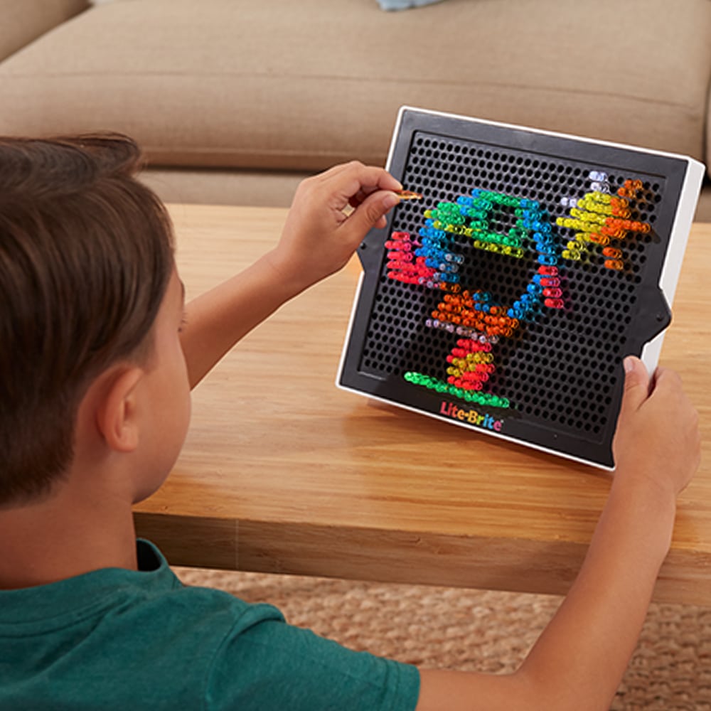 Child playing with Lite Brite creating a colorful light art design using pegs on a black pegboard.