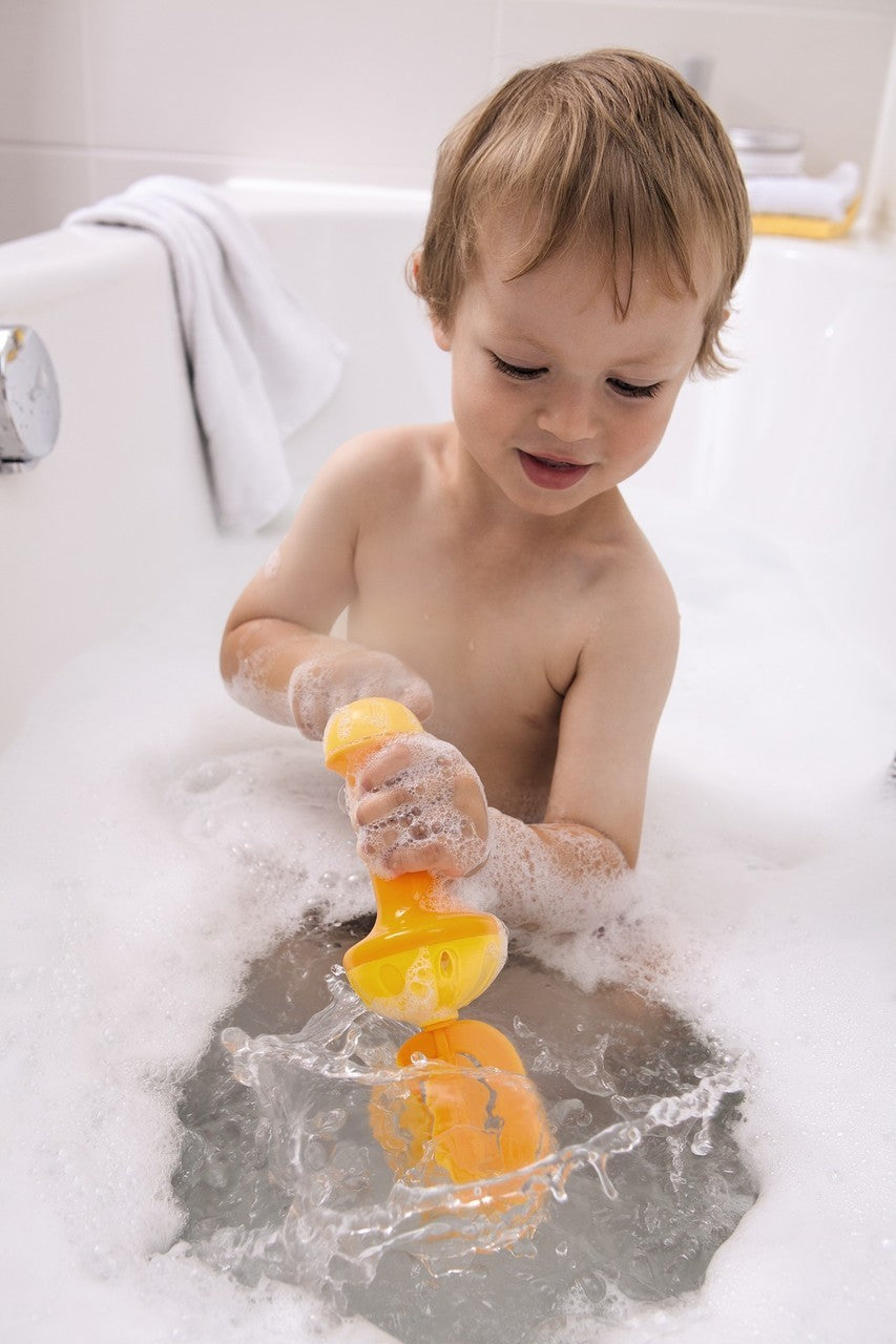 Child playing with yellow Bubble Bath Whisk in foam-filled bathtub creating bubbles and splashing water.