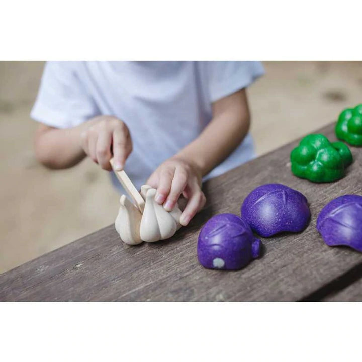 Child playing with the Five Color Veggie Set, slicing garlic and colorful veggies on a wooden surface.