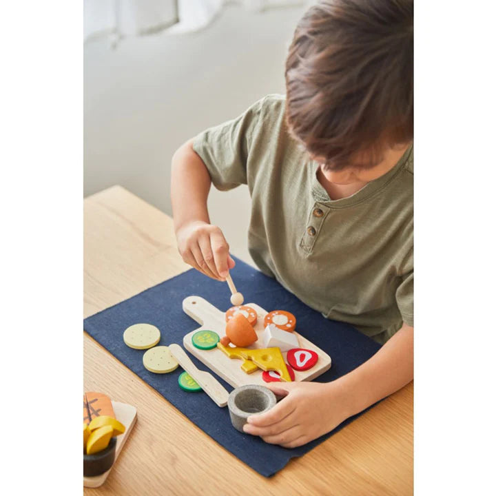 Child preparing a European appetizer with a Charcuterie Board set including cheese, salami, cucumbers, and knife.