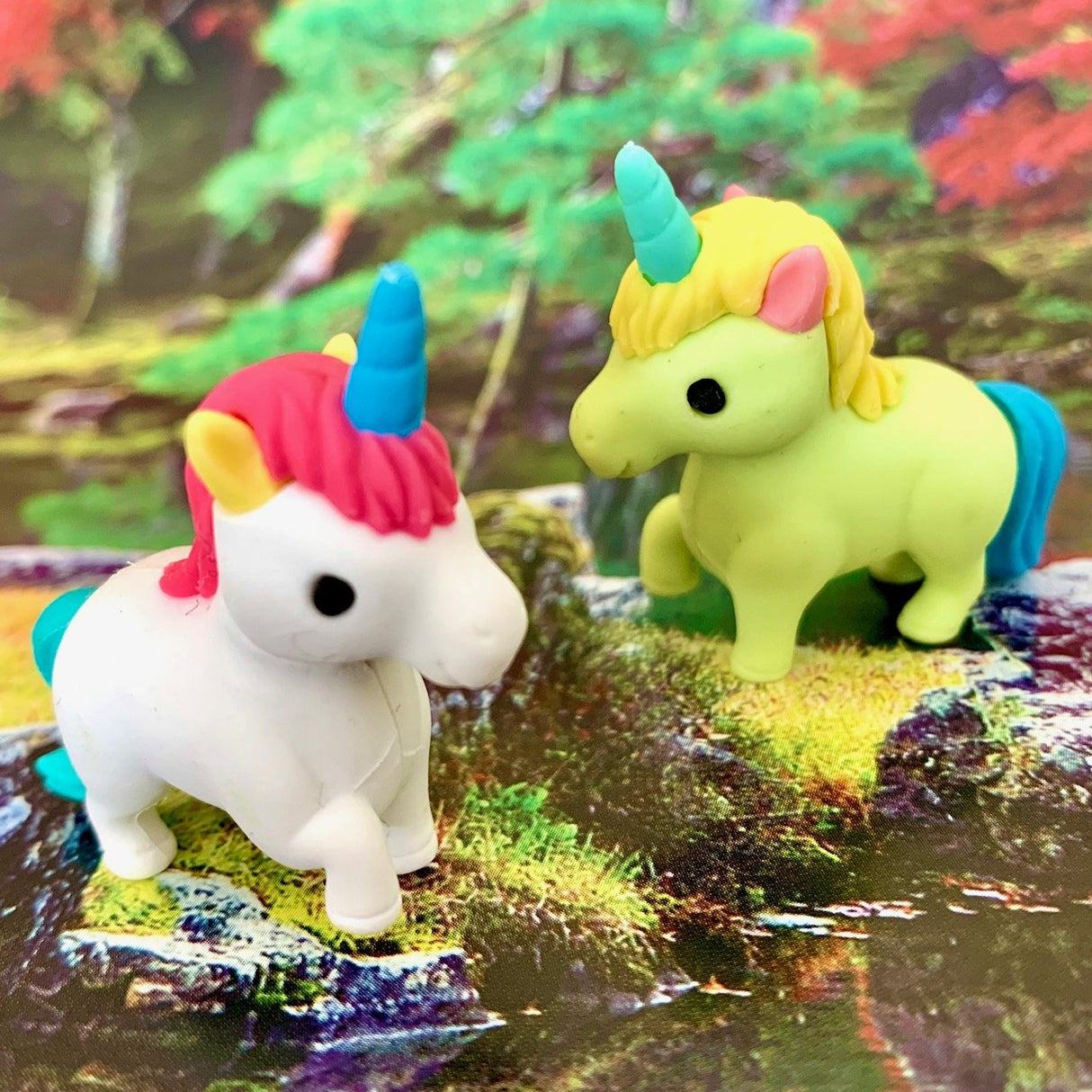 Two colorful Japanese Eraser Unicorn puzzle erasers with detachable parts on a nature-themed background.