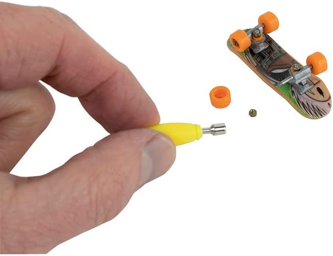 Hand assembling the World's Smallest Tech Deck fingerboard with a yellow tool and small parts on white background.