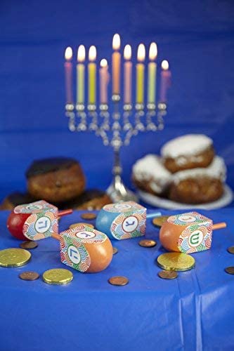 Dreidel | Colorful Wooden spinning top on blue cloth with chocolate coins and Hanukkah menorah candles in background