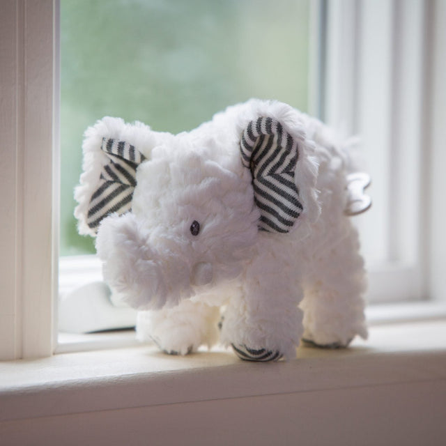 White plush elephant with striped ears sitting on a windowsill, Afrique Elephant Musical toy.