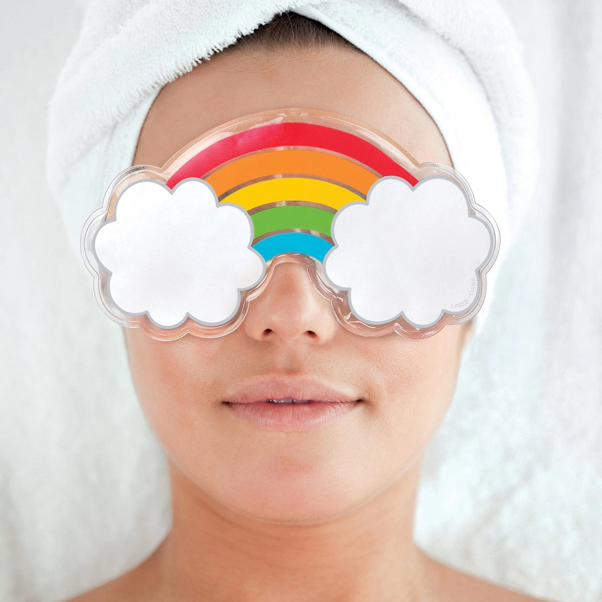 Woman relaxing with Chill Out! Eye Mask Rainbow featuring colorful rainbow and cloud design for puffy eyes relief