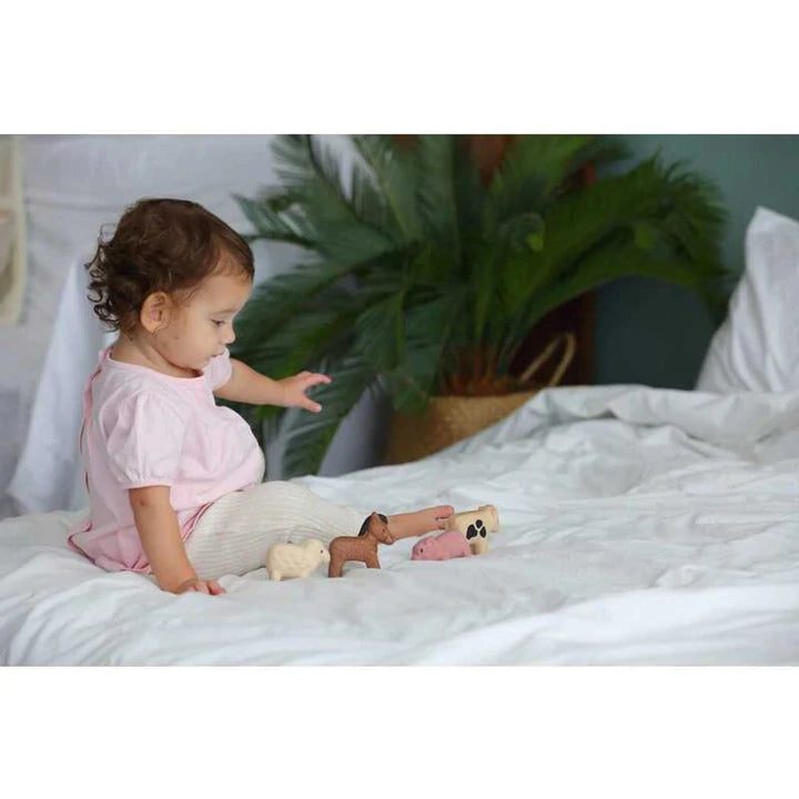 Child playing with cute wooden Farm Animals including pig, sheep, cow, and horse on a white bed.