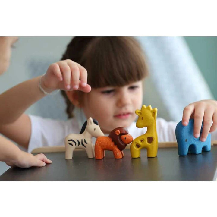 Child playing with colorful wooden Wild Animals set including lion, elephant, zebra, and giraffe on a table.
