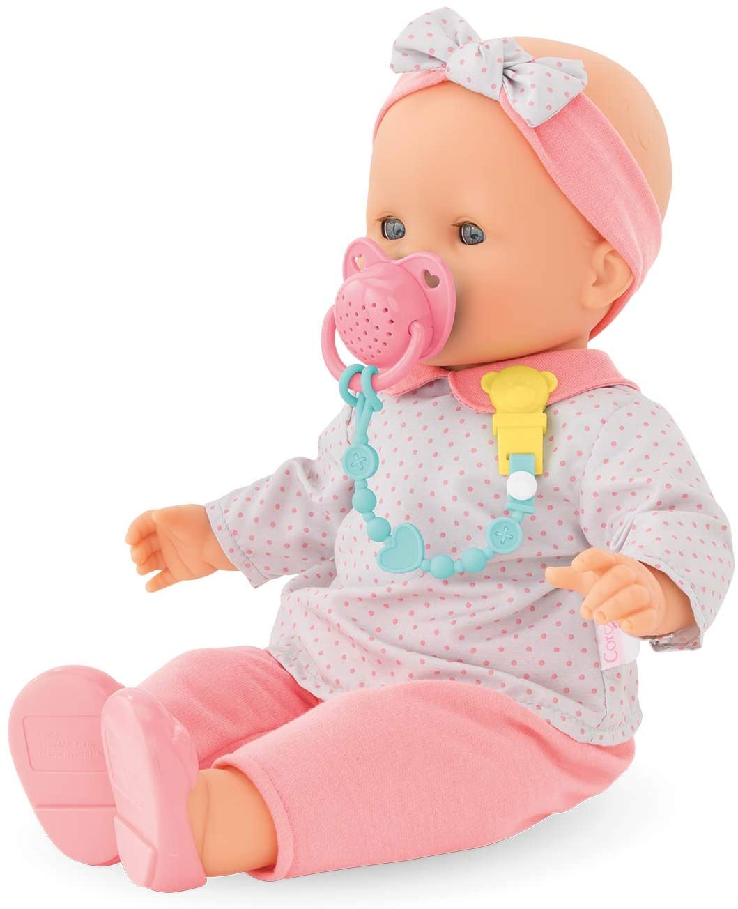 Pacifier with Sounds on baby doll wearing pink outfit and headband with pacifier clip attachment.