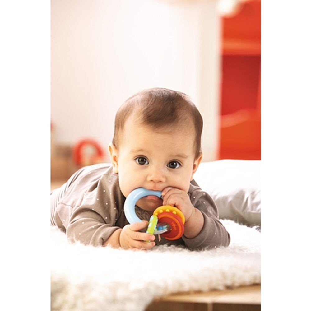 Baby lying on tummy chewing colorful Clutching Nobbi Teether with textured silicone rings and rattle element.