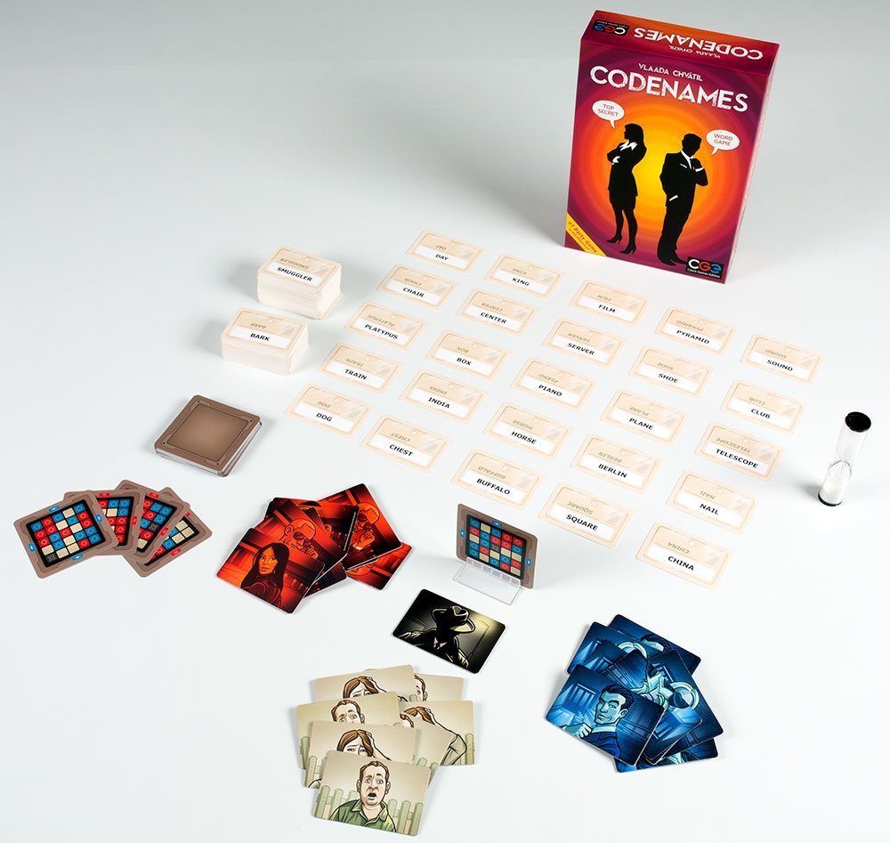 Codenames board game with word cards, clue cards, key card, sand timer, and box on white surface.