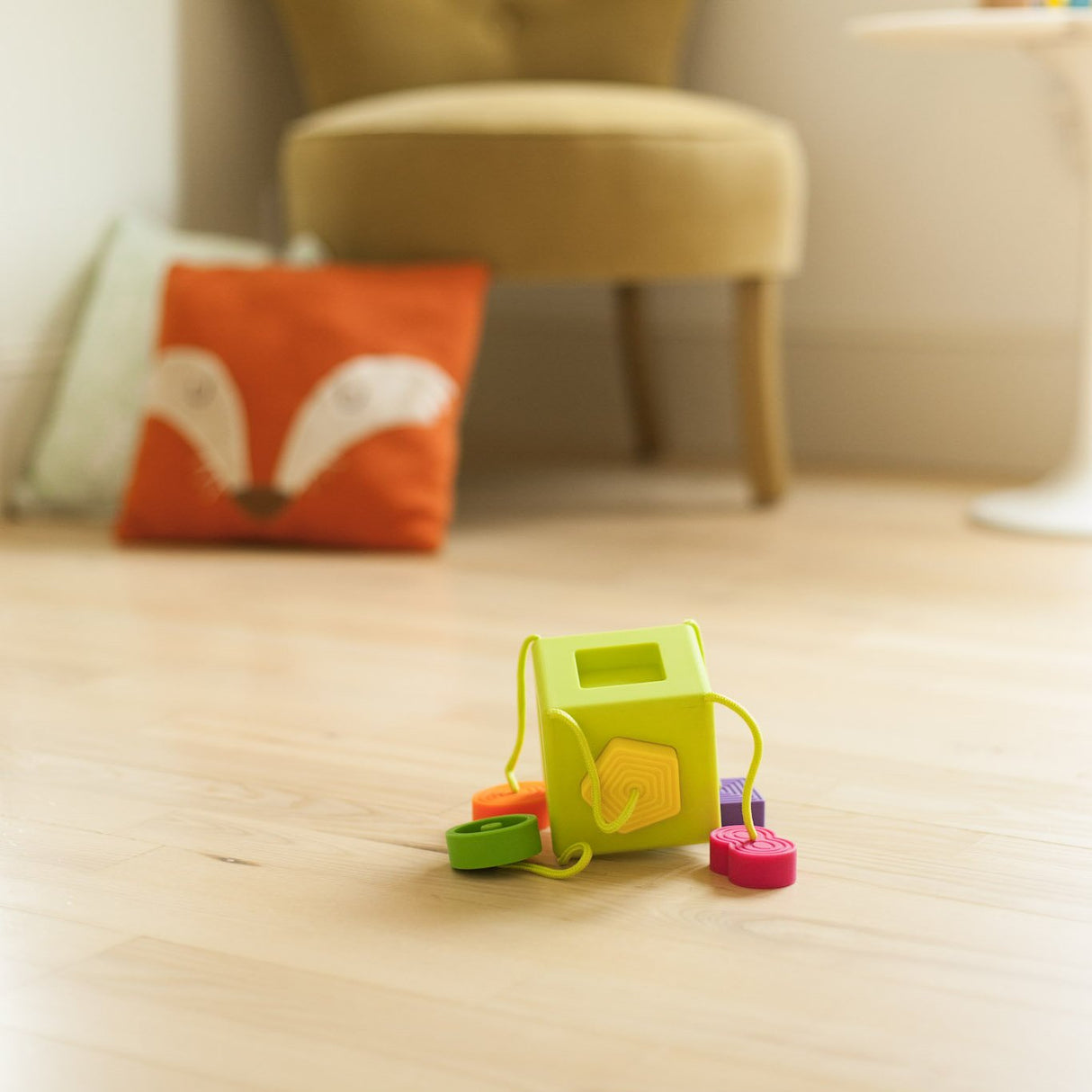 OombeeCube with six colorful, textured tethered shapes for tactile exploration and sensory learning on a wooden floor.
