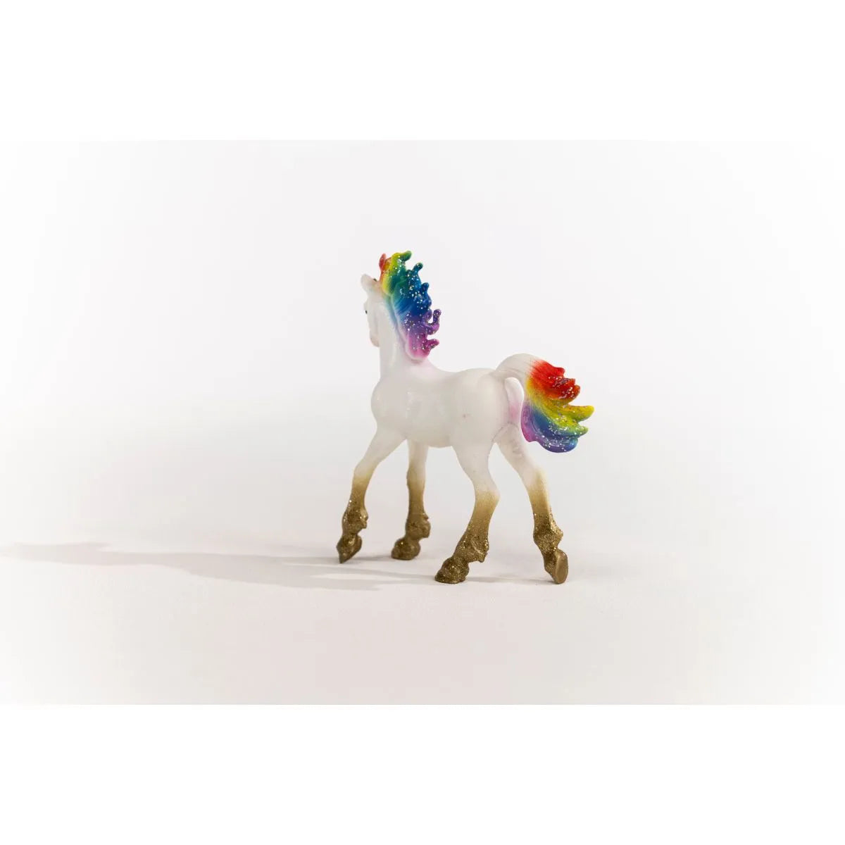 Bayala | Rainbow Love Unicorn Foal with shimmering gold legs and vibrant rainbow-colored mane and tail on white background.