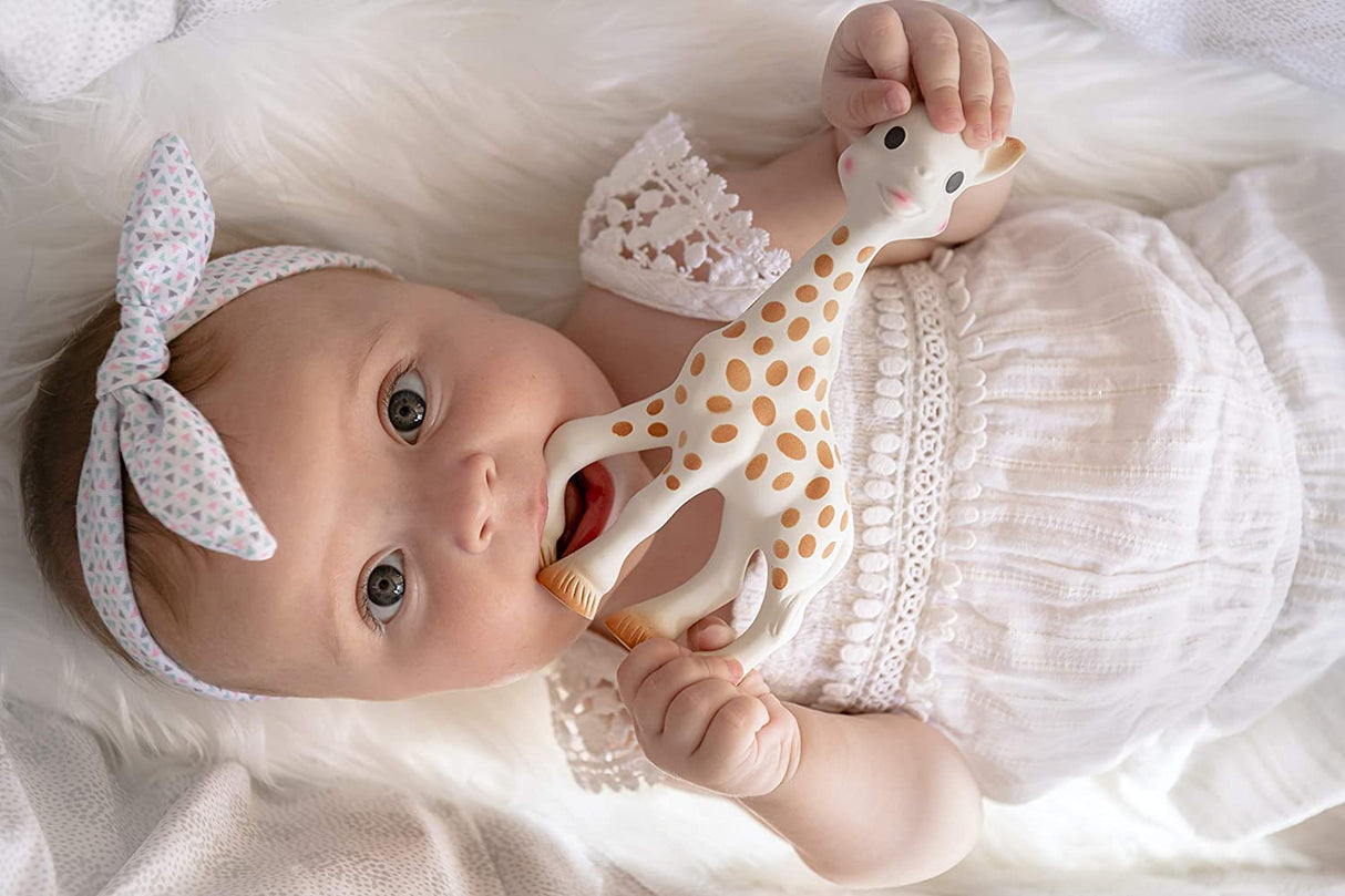 Baby lying down chewing on Sophie the Giraffe natural rubber toy, perfect for sensory play and tiny hands grasping.
