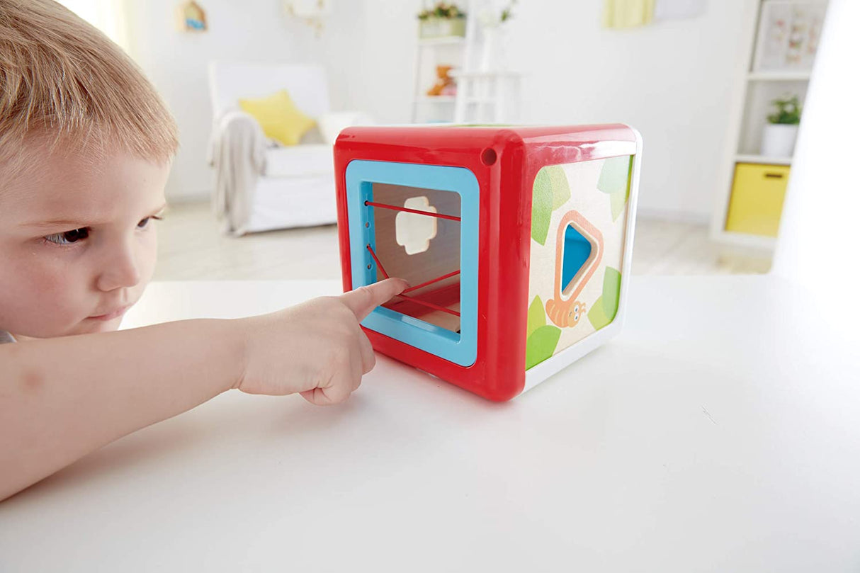 Child playing with the Shape Sorting Box, matching shaped pegs to corresponding garden creature holes on the wooden cube.