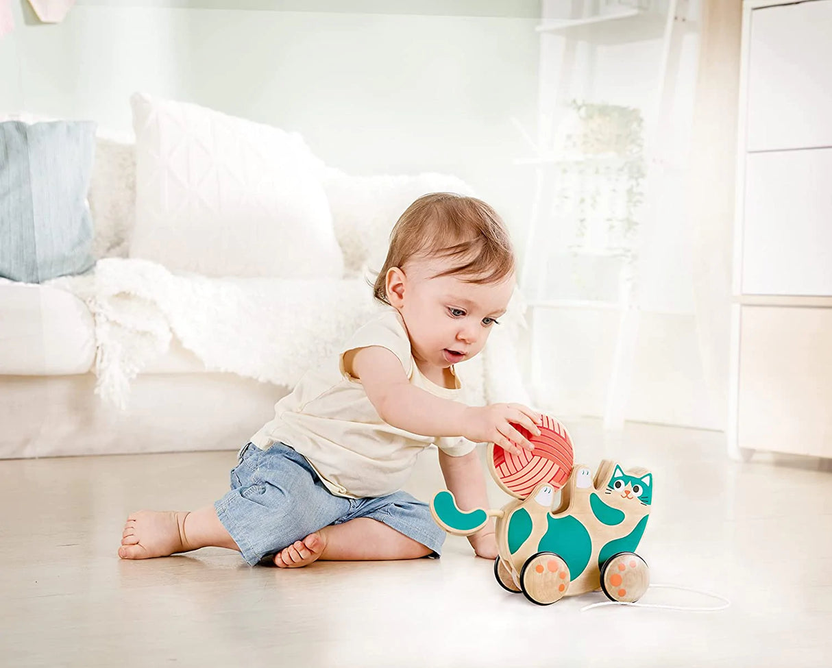 Baby playing on floor with Pull Along Roll & Rattle Kitten wooden toy holding a removable wool rattle ball.