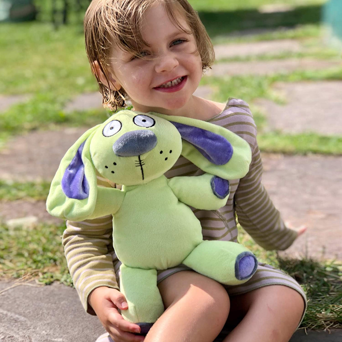 Child smiling outdoors holding a green plush toy dog, not the Knuffle Bunny product.