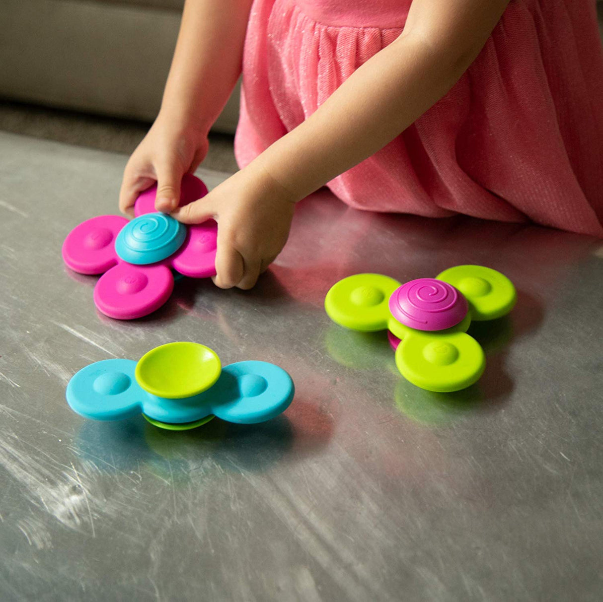 Child playing with colorful Whirly Squigz silicone spinners designed for sensory and motor skill development.