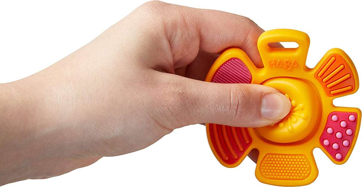 Hand holding bright orange and pink Popping Flower Silicone Teething Toy with textured petals and pop center button.