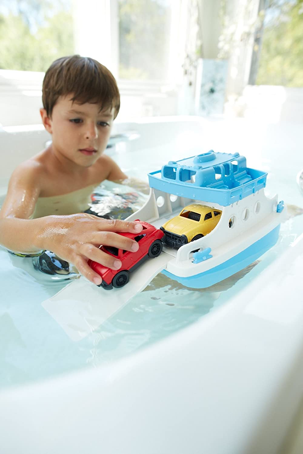 Child playing with the Ferry Boat toy in a bathtub, loading small colorful cars onto the two-story vessel.