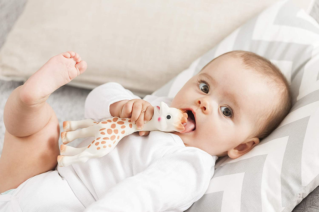 Baby lying down chewing on Sophie the Giraffe natural rubber teething toy sized for tiny hands.