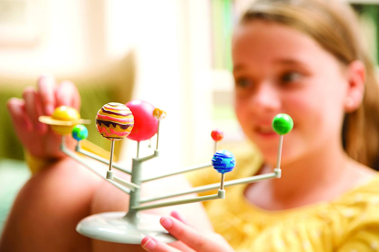 Young girl assembling and exploring the 4M Solar System Planetarium with colorful planets and sun model.