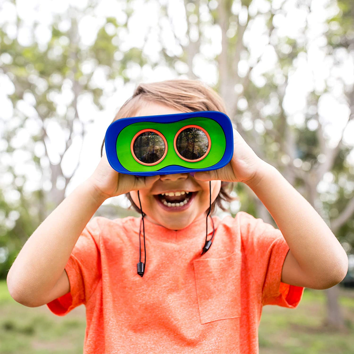 Child smiling outdoors using Kidnoculars Binoculars with bright blue and green focus-free eyepieces and neck strap.