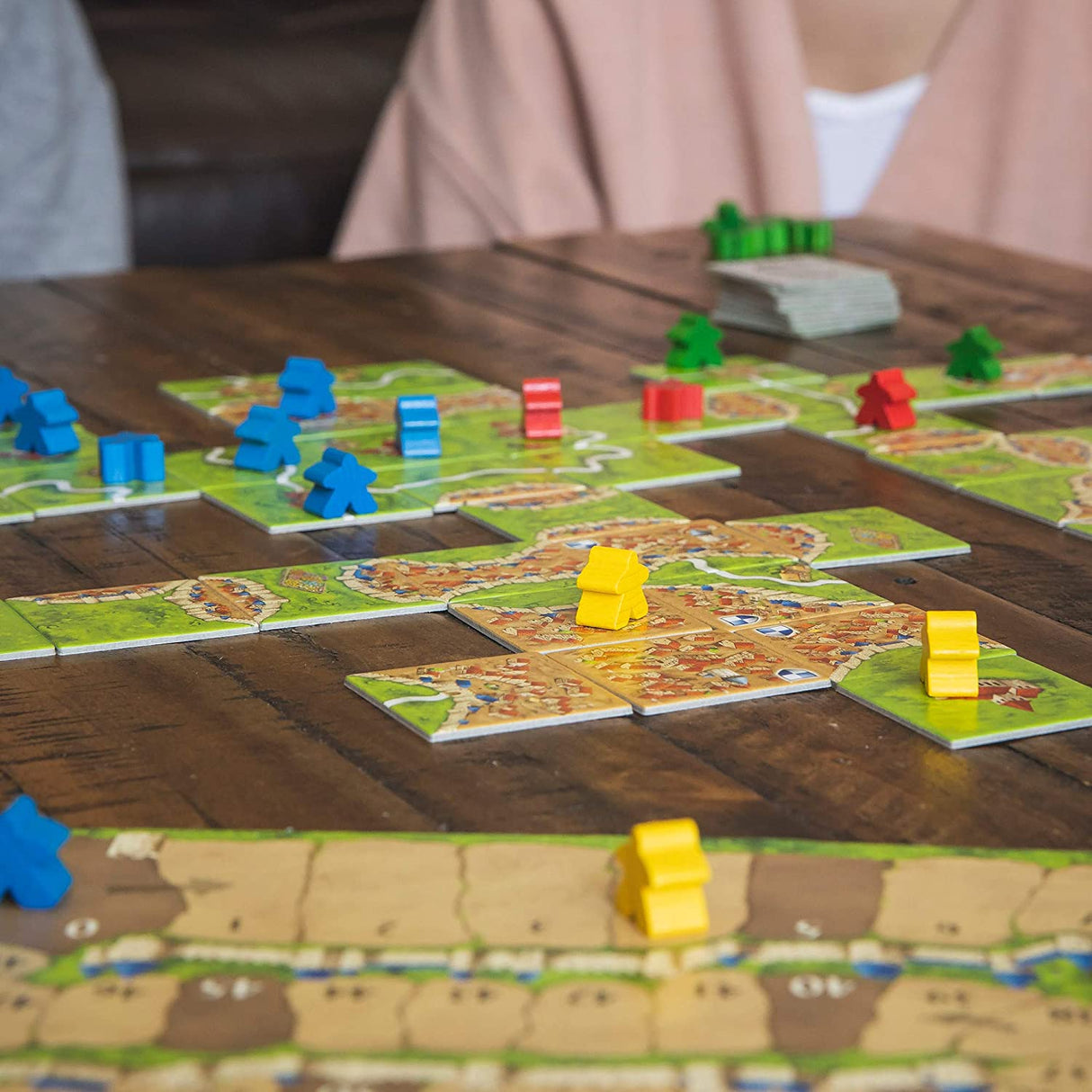 Carcassonne board game with colorful tiles and followers creating a medieval fortress landscape on a wooden table.