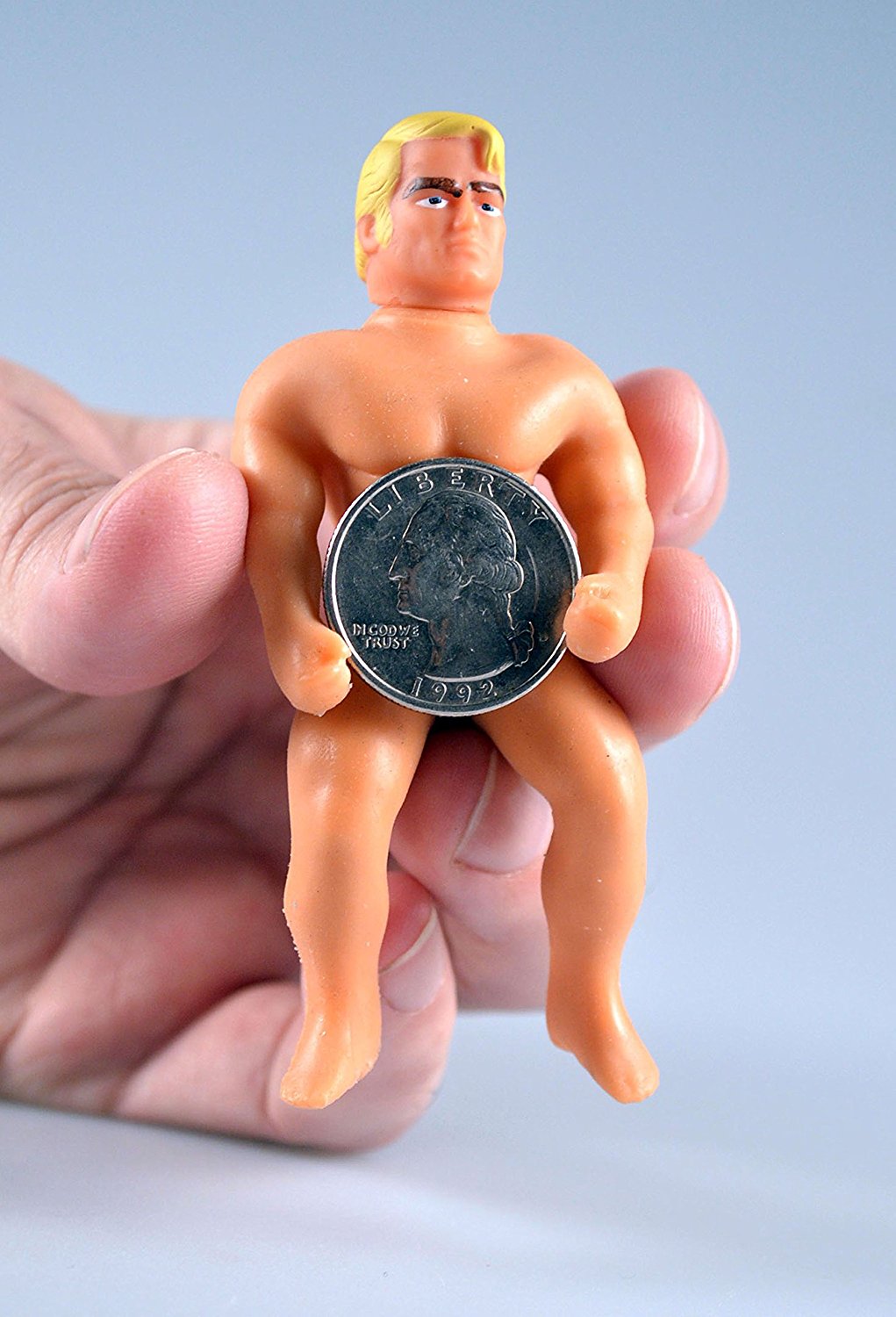 Hand holding the World's Smallest Stretch Armstrong toy with a quarter showing its tiny size and muscle detail.