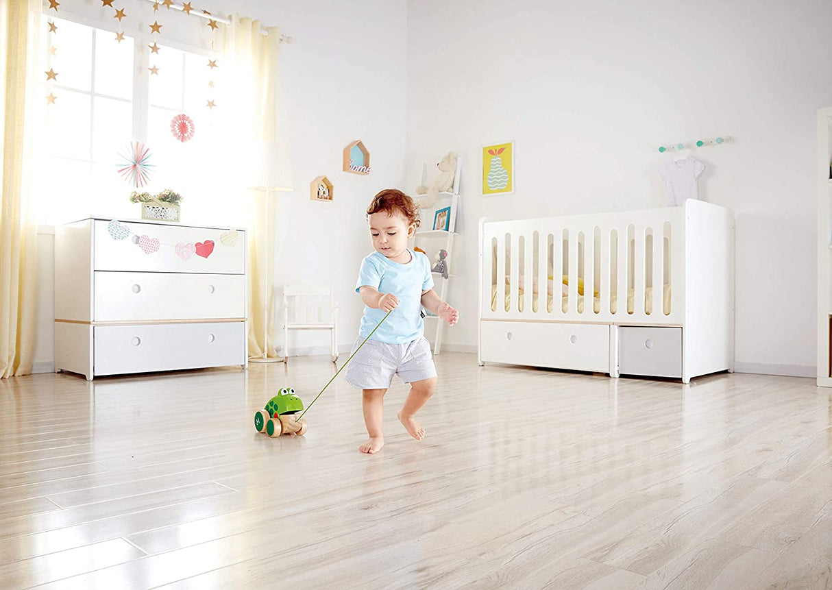 Child pulling the Pull Along Frog toy with mouth opening and closing in a bright nursery room.