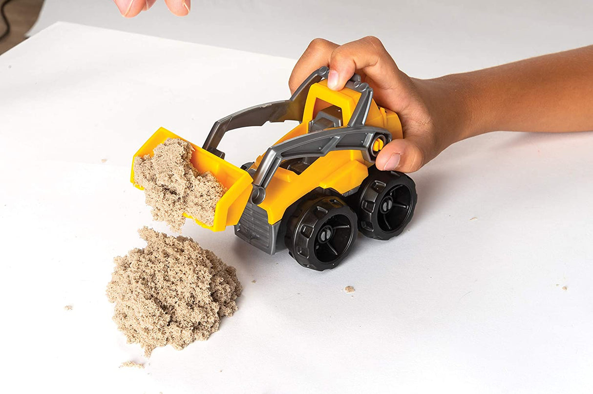Child playing with a yellow construction truck scooping brown Kinetic Sand Dig & Demolish on a white surface.