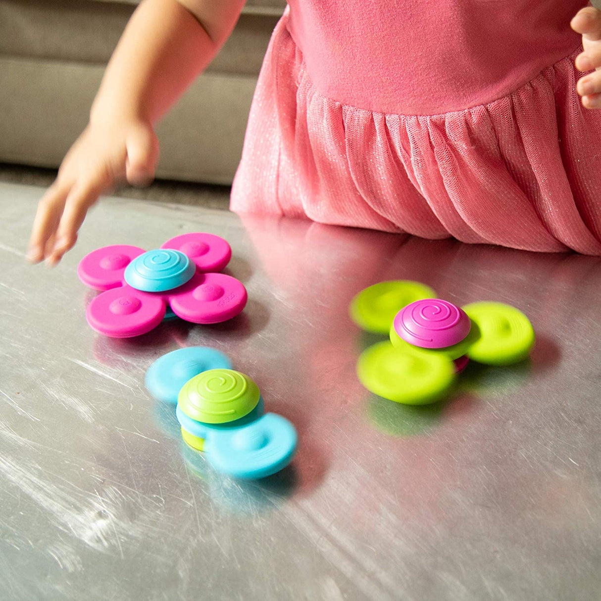 Child playing with colorful silicone Whirly Squigz spinners on a smooth tabletop surface.