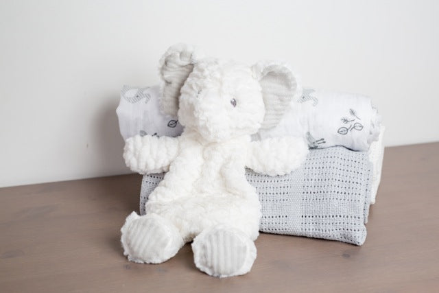 Afrique Elephant Lovey with white textured body and embroidered eyes sitting on folded blankets.