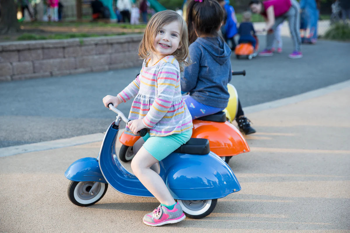 Child riding a blue self-propelled scooter toy Primo Ride On Blue in a park setting.