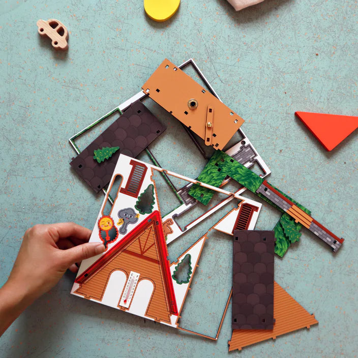 Hand assembling colorful pieces of the Make Your Own Weather House DIY kit on a blue surface.