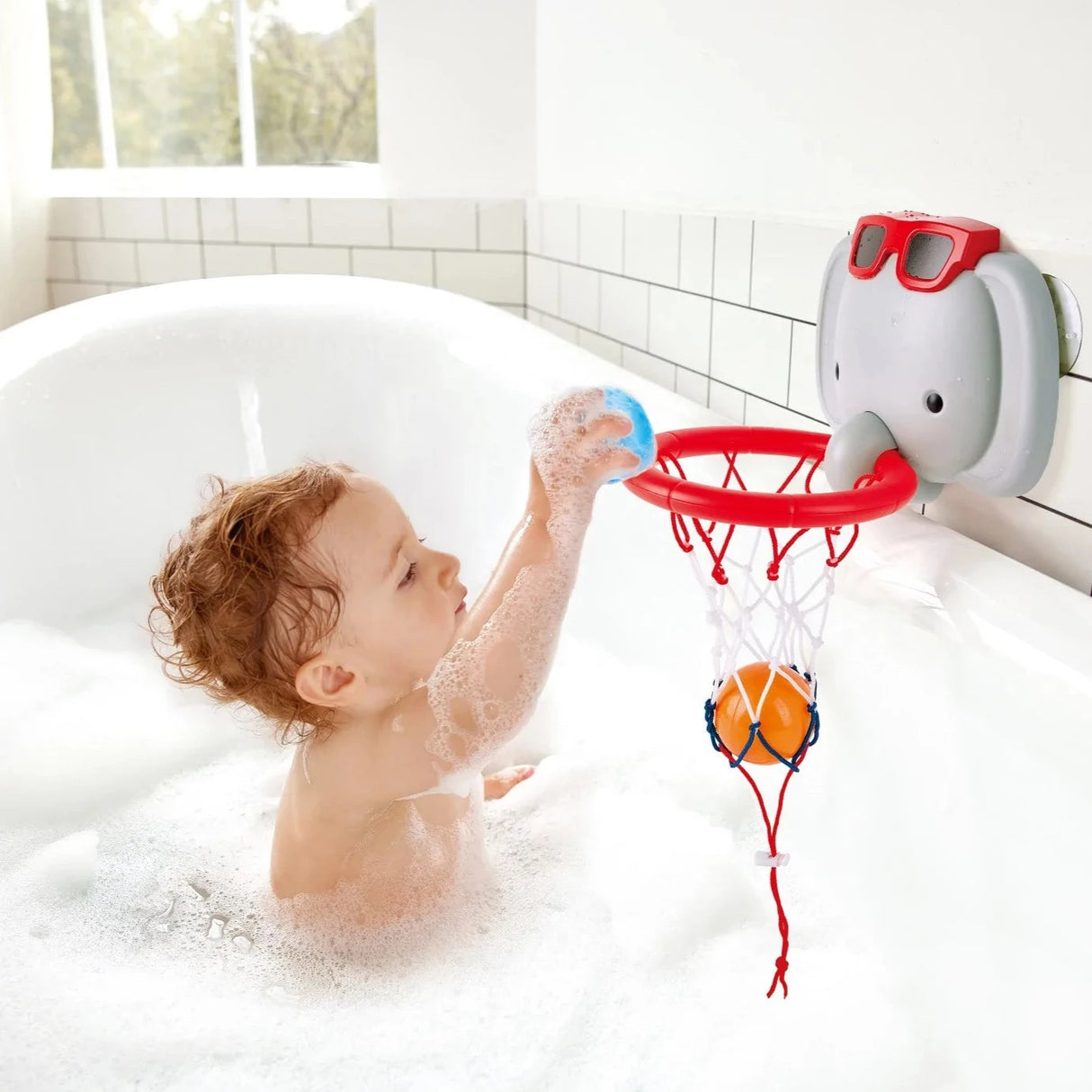 Child playing with the Elephant Pal Basketball in a bubble bath, shooting colorful floating balls into the hoop.