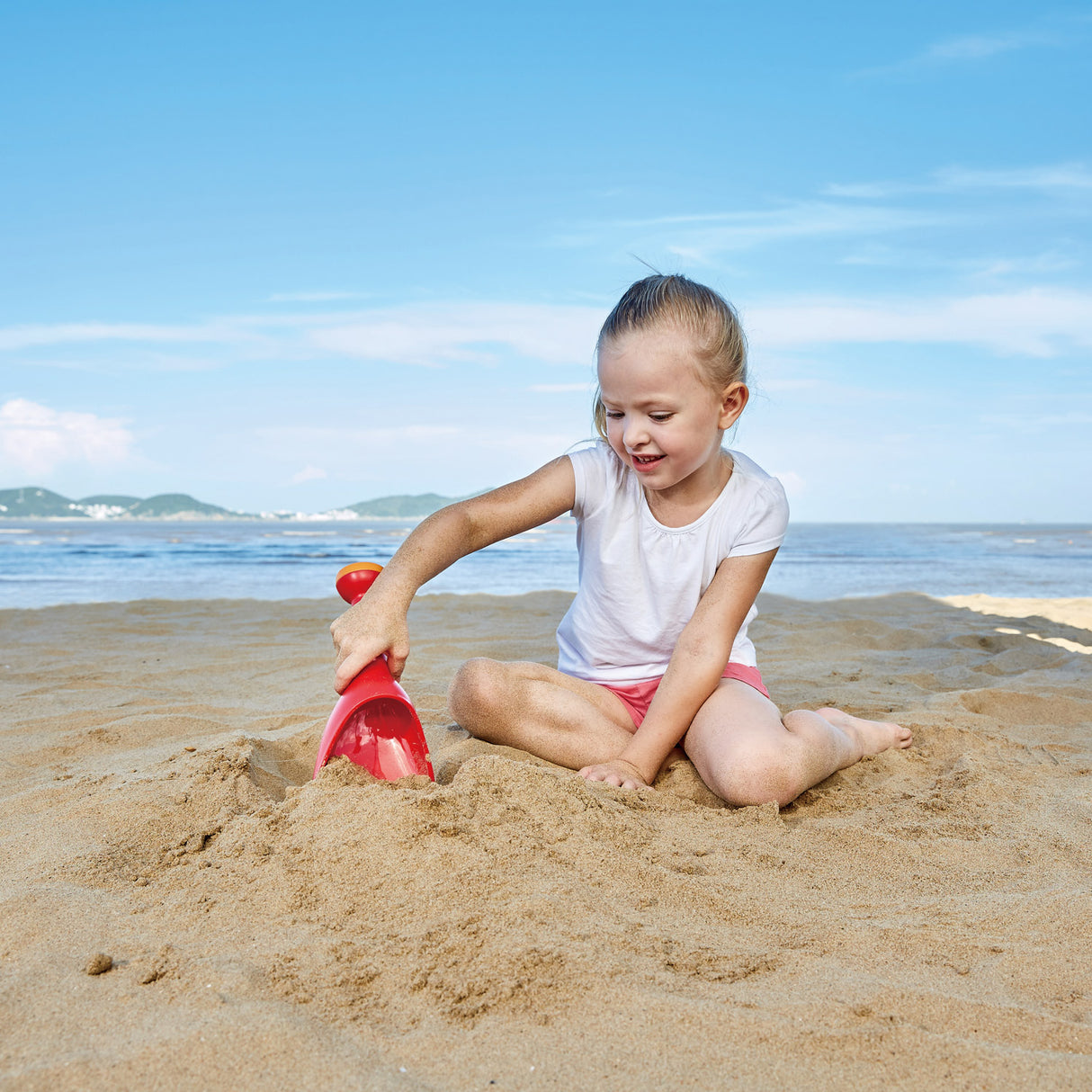 Child playing on the beach with a red Rain Shovel Red, perfect for sand and water play outdoors.