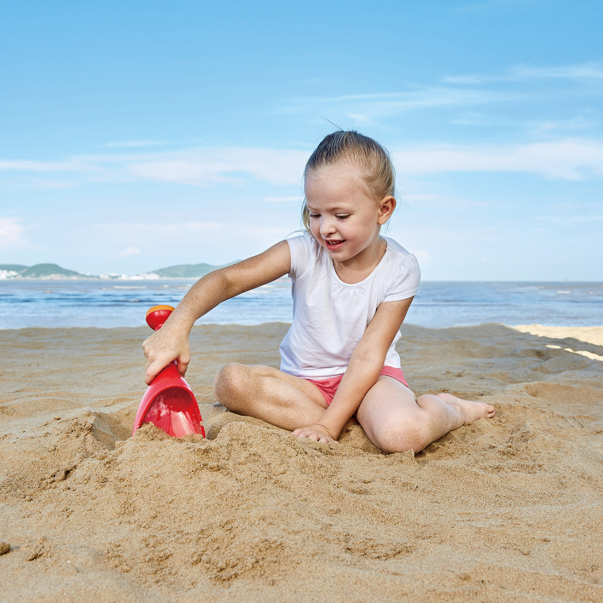Child playing on the beach with a red toy shovel, not the Rain Shovel Blue product shown in the listing.