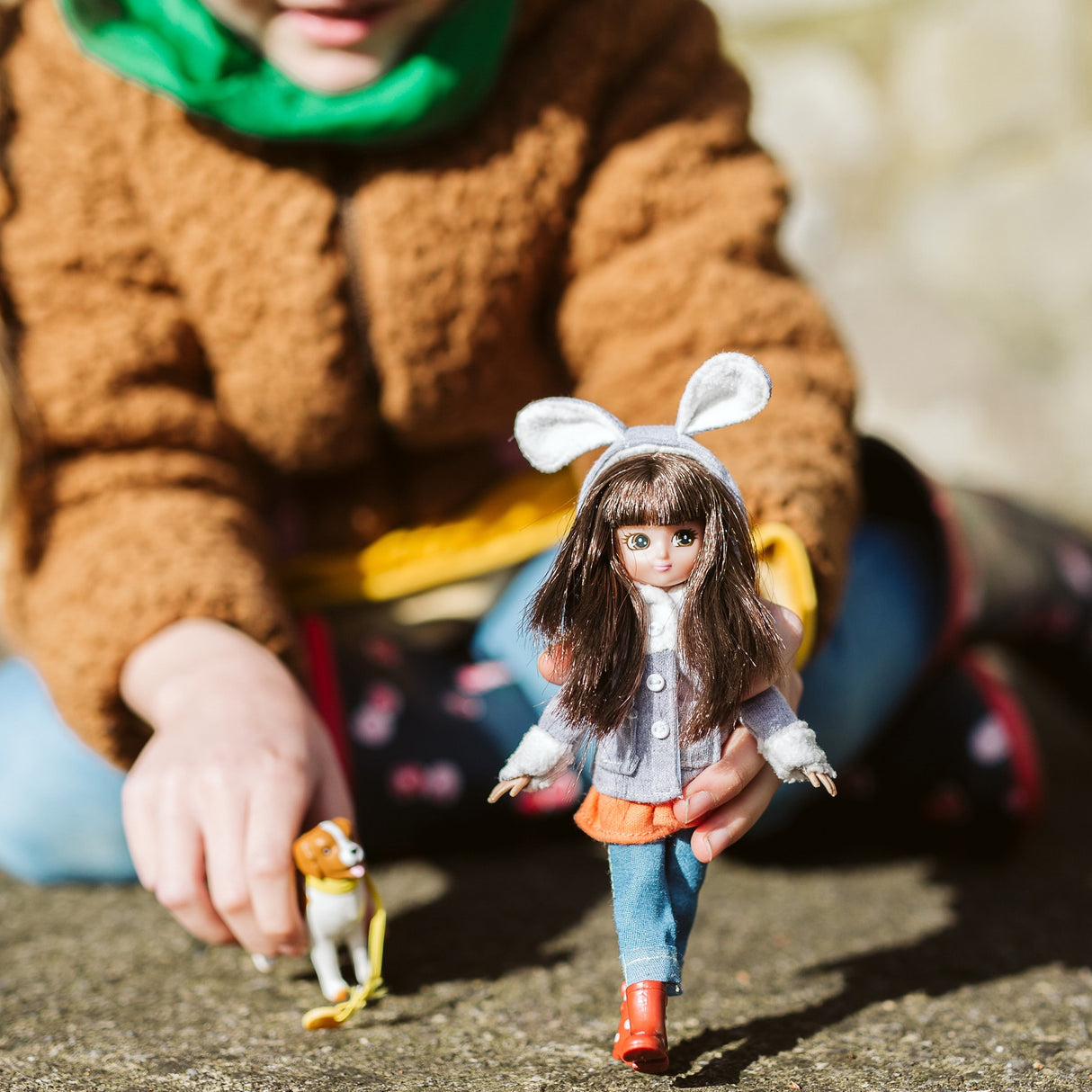 Lottie Walk in the Park doll wearing bunny coat and boots, walking with pet dog held by a child outdoors.