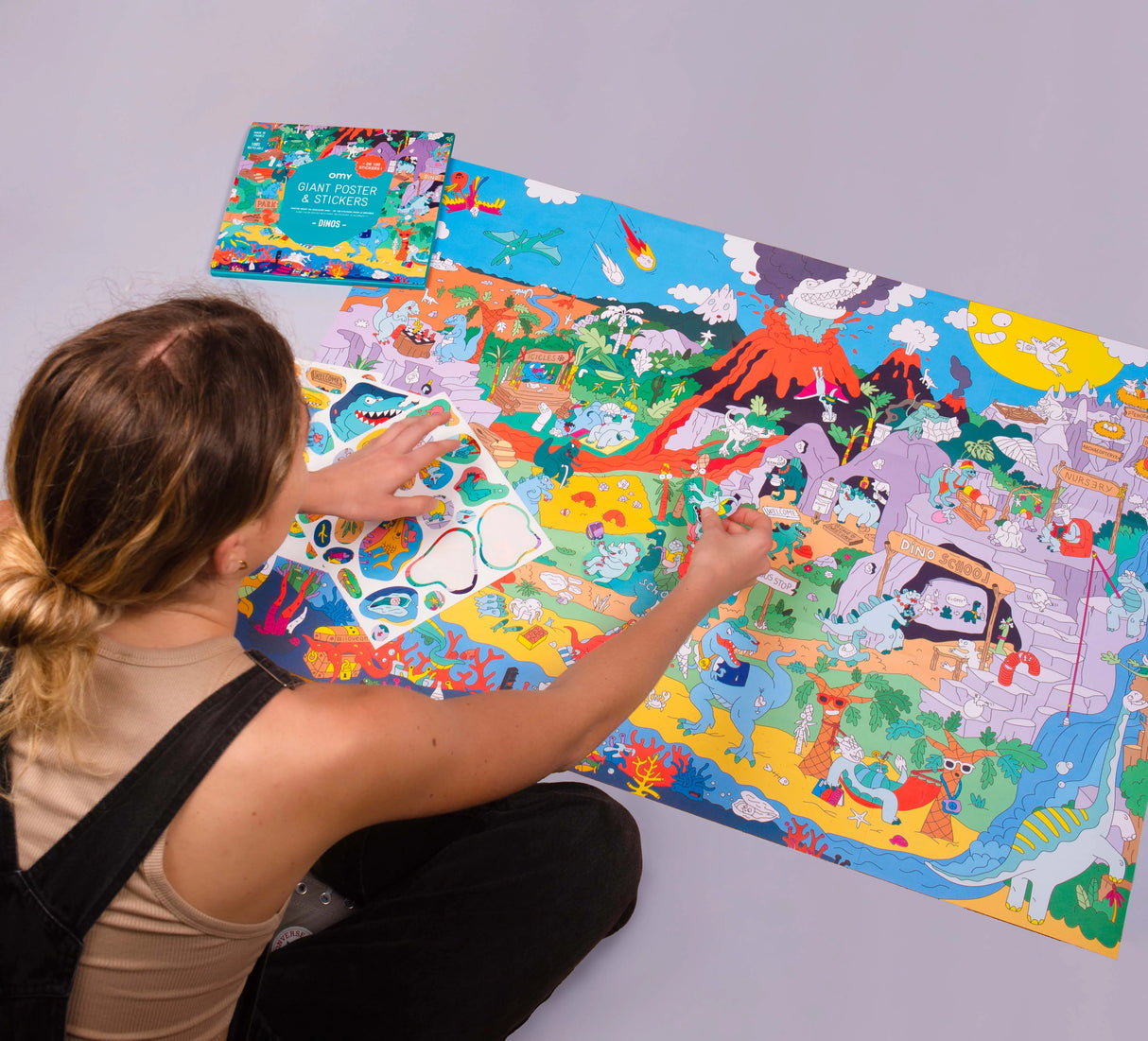 Person sticking colorful stickers on Dinosaur Giant Sticker Poster with vibrant dinosaur scene and volcano background.