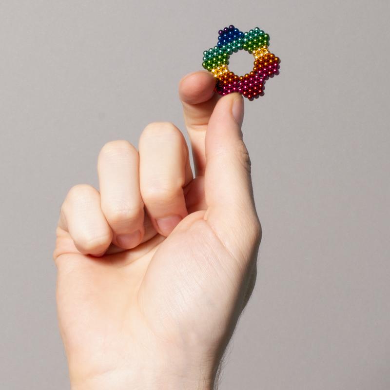 Hand holding a colorful ring made of Speks. Spectrum. magnetic balls, a fun stress-relief desk toy.