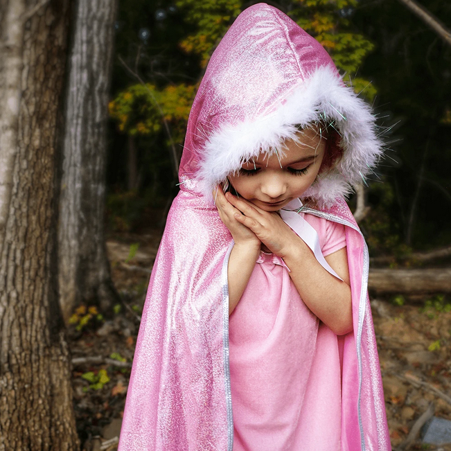 Child wearing a pink Glitter Princess Cape with white marabou trim and hood, featuring a satin bow and large gem.