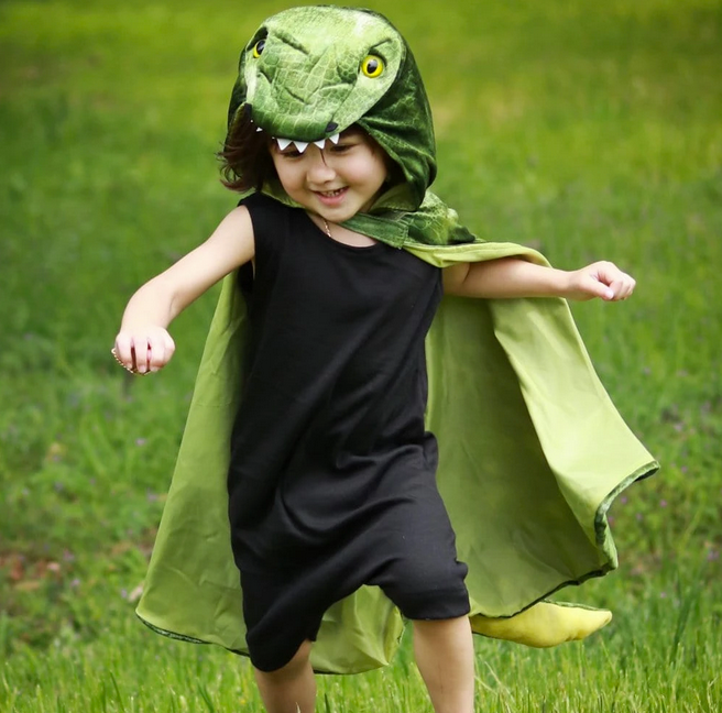 Child happily running outdoors wearing the T-Rex Hooded Dinosaur Cape with textured velour and 3D detailing.