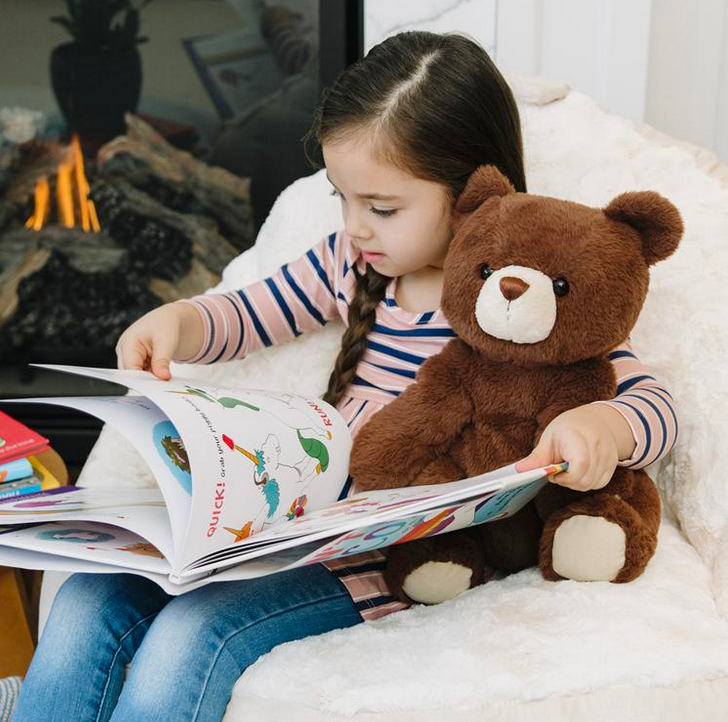 Child reading a book while holding a 13-inch seated dark brown teddy bear Finley with soft plush fur.