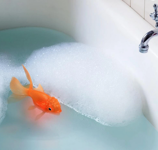 Koi Toy Light Up Goldfish floating in bubble-filled bathtub, glowing brightly with realistic orange details, 7.5 inches long.