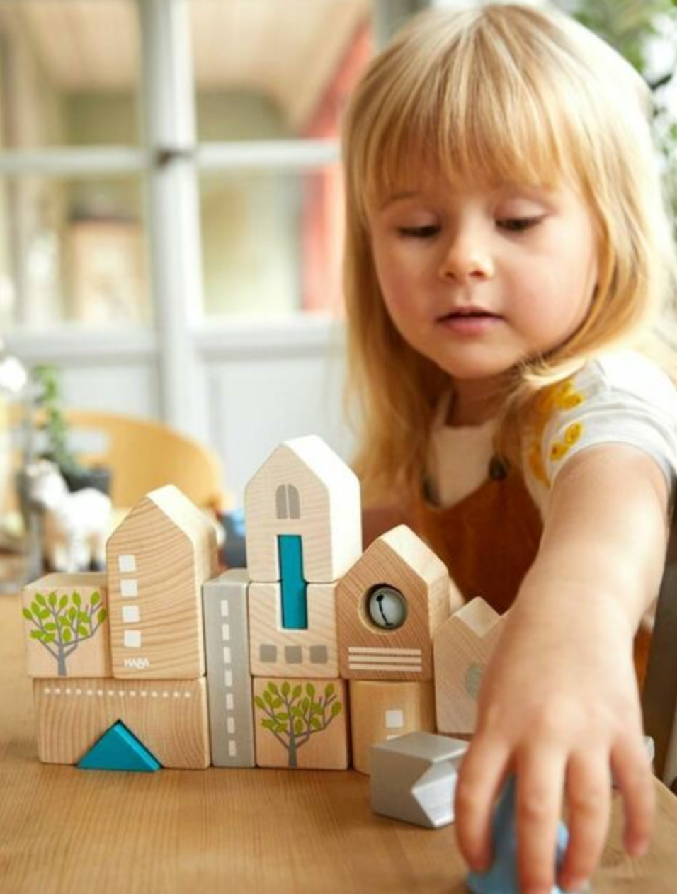 Young child playing with Bad Rodach Wooden Building Blocks made of beech wood, featuring town skyline elements.