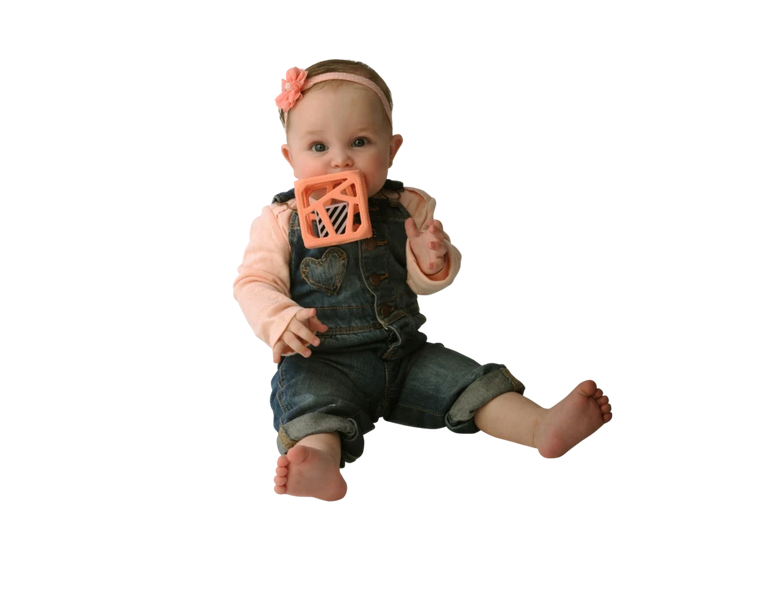 Baby chewing on a soft textured peachy pink Chew Cube | Peachy Pink teether and rattle toy.